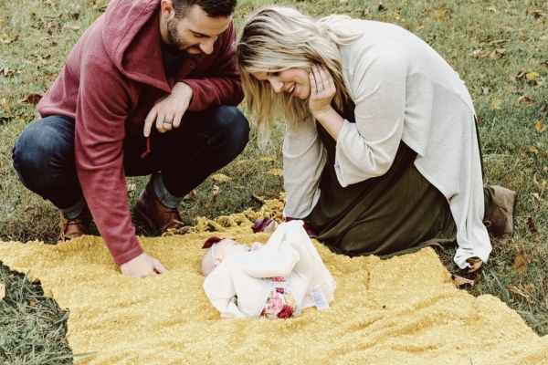 man and woman looking at baby on picnic maty