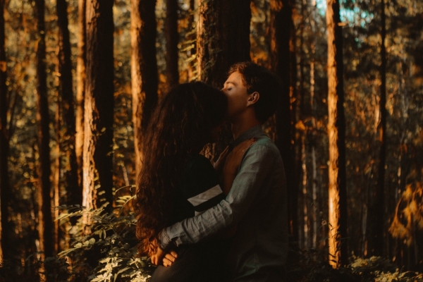 man kissing woman's forehead in forest