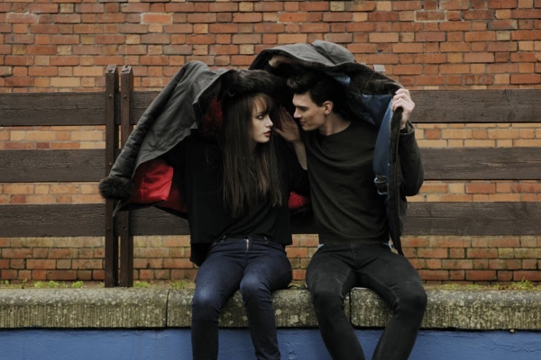 Man and Woman Sitting on Bench While Covering Heads With Jackets