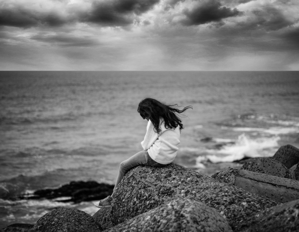 grayscale photography of woman sitting near body of water