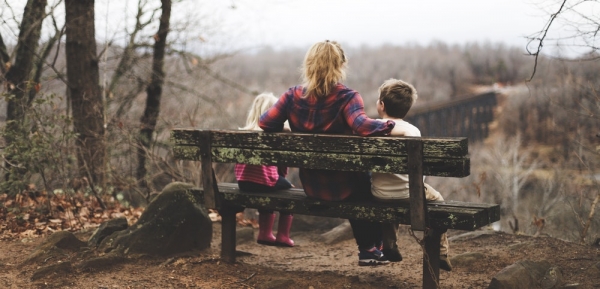 woman between two childrens sitting on pown wooden bench during daytime