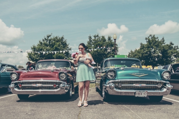 woman carrying child standing between two vintage cars